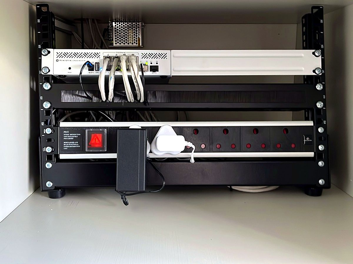 Small network rack inside a cupboard with a switch, patch leads and a power distribution strip